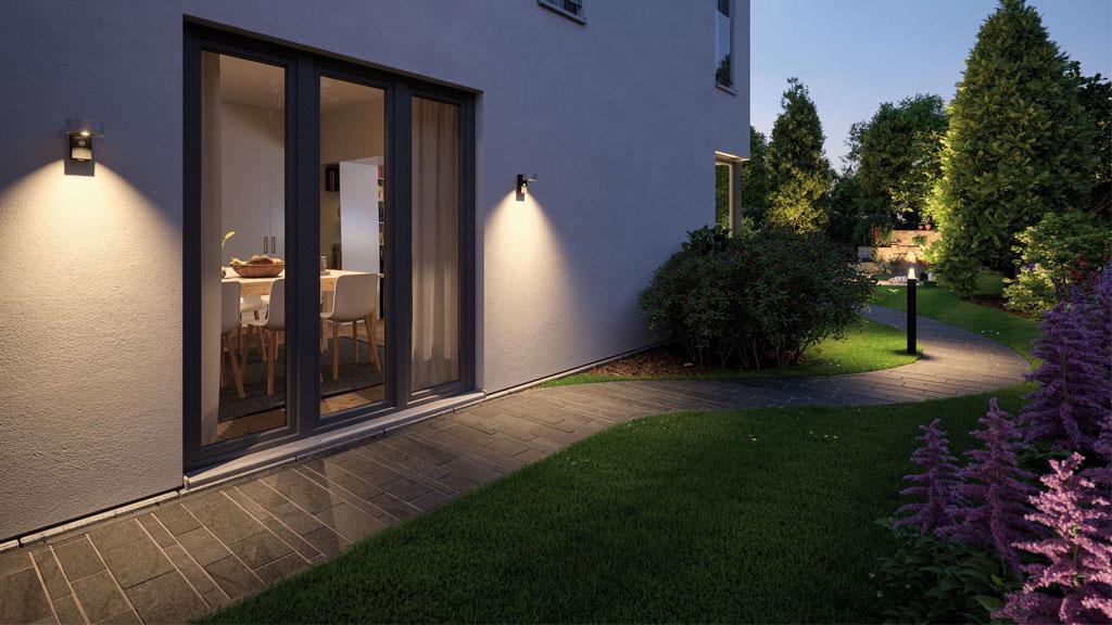 Moderne Außenbeleuchtung mit warmweißem Licht an Hauswand und Gartenweg bei Abenddämmerung.