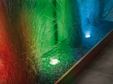 Eingelassene LED-Bodenleuchten in Edelstahl mit farbigem Licht auf Kiesbett und Gräsern im Garten