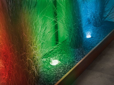 Recessed stainless steel LED floor lights with colored illumination on gravel and garden grasses