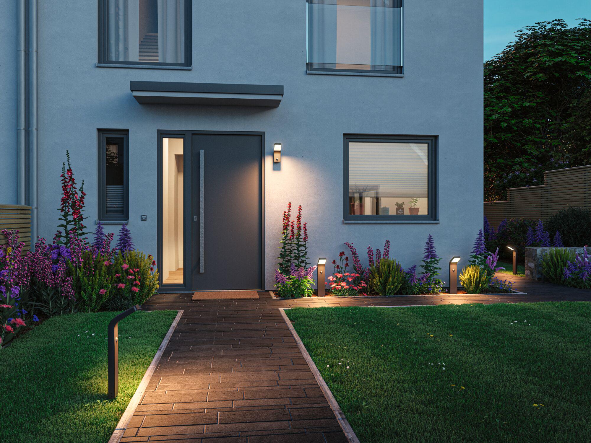 Moderne Außenbeleuchtung mit schwarzen LED-Wegeleuchten und Wandlampen an Haus mit Gartenweg und Blumen.