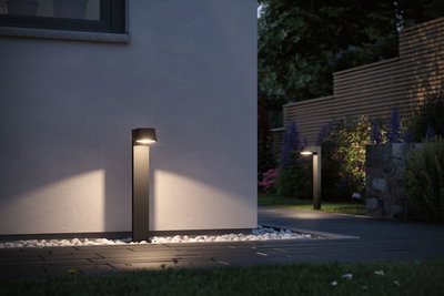 Modern black metal LED outdoor light illuminating garden path with warm white light.
