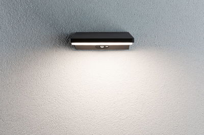 Black metal LED wall light with motion sensor mounted on white wall for outdoor lighting