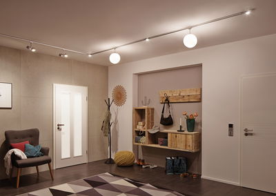 Moderne hal met houten plank, grijze fauteuil, gele poef en plafondlamp met witte bollen