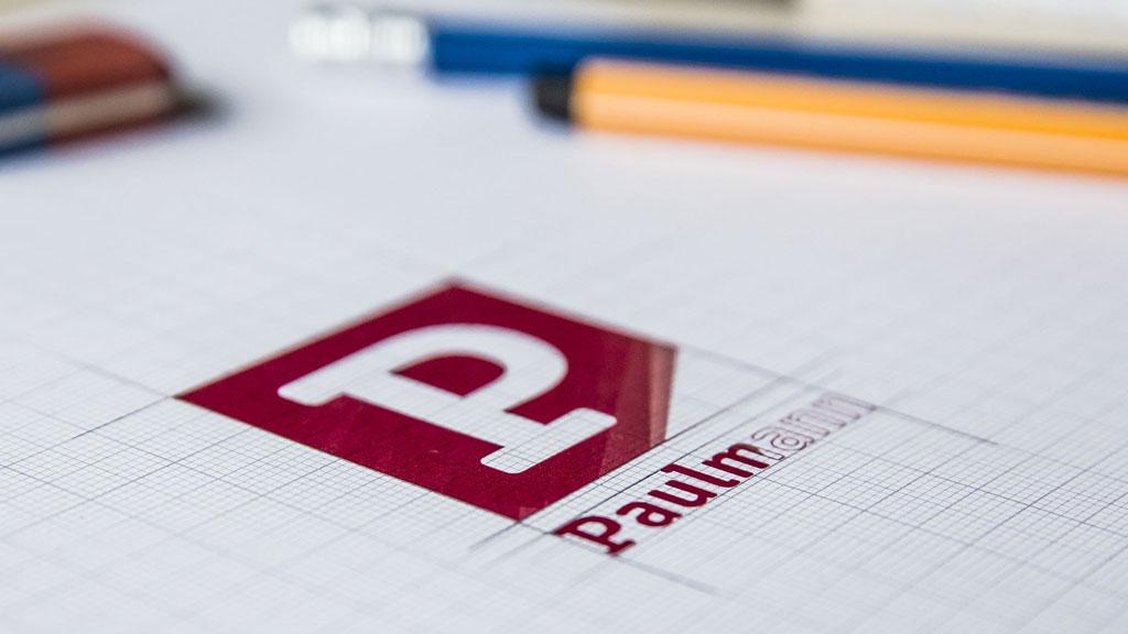Rotes Paulmann-Logo auf kariertem Papier mit Bleistift und Radiergummi im Hintergrund