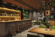 Modernes Barinterieur mit Holztheke, grünen Sesseln, Pflanzen und schwarzen Pendelleuchten für stimmungsvolle Beleuchtung