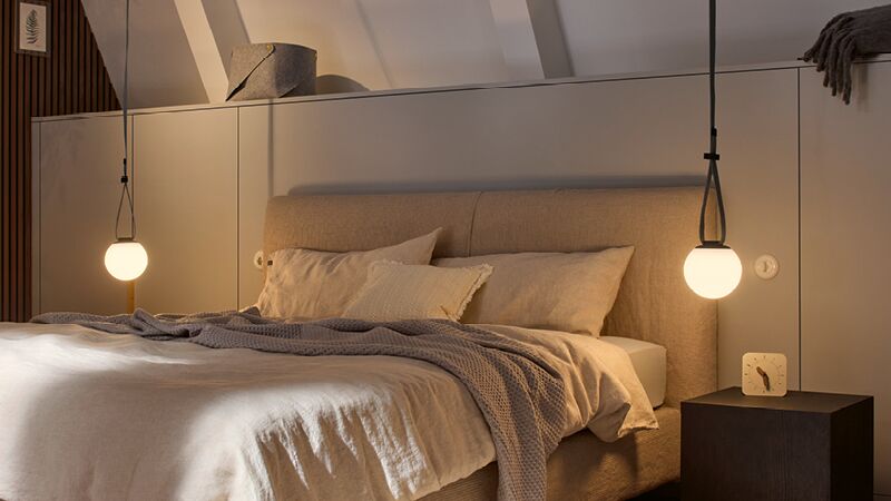 Gemütliches Schlafzimmer mit beigem Stoffbett, warmweißen Hängelampen und dunklem Nachttisch für moderne Beleuchtung