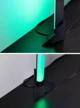 Zwarte LED-vloerlamp met groen licht op donkere houten tafel, modern ontwerp met kabel