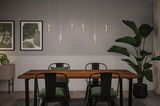 Modern dining area with wooden table, black metal chairs, and six hanging LED bulbs emitting warm light.