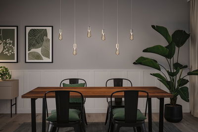 Modern dining area with wooden table, black metal chairs, and six hanging LED bulbs emitting warm light.