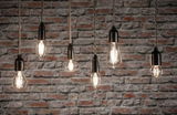 Six ampoules LED filament claires de formes variées suspendues devant un mur en briques rouges pour éclairage décoratif