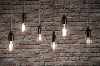Six clear filament LED bulbs in various shapes hanging against red brick wall for decorative lighting