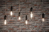 Six clear filament LED bulbs in various shapes hanging against red brick wall for decorative lighting