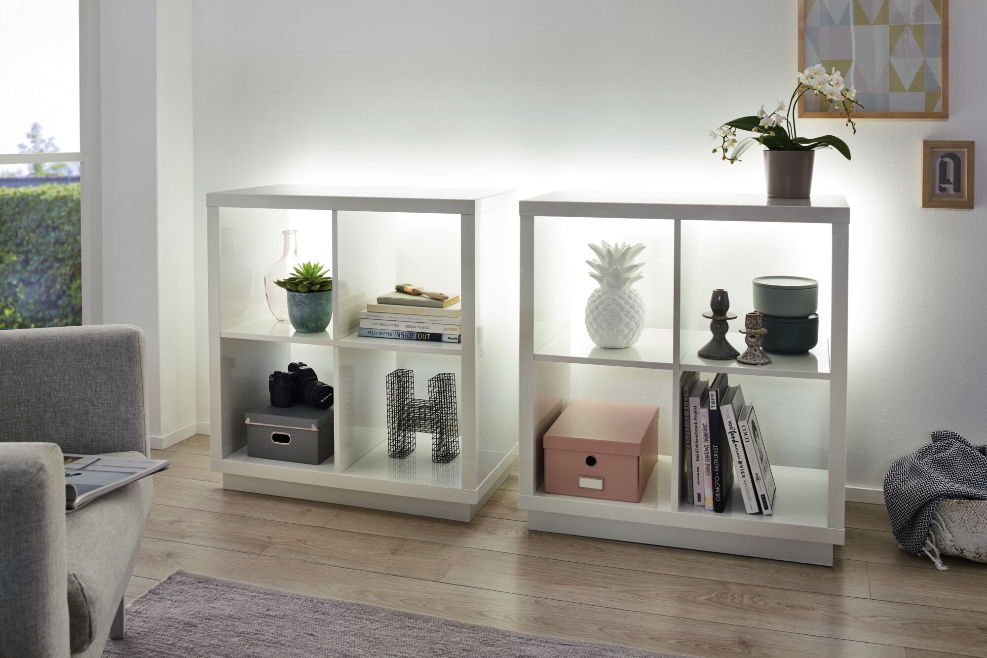 To hvide reoler med LED-belysning, dekoreret med bøger, pynt og planter i stuen.