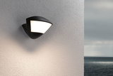Black outdoor wall light with white diffuser on textured wall, modern LED exterior lighting