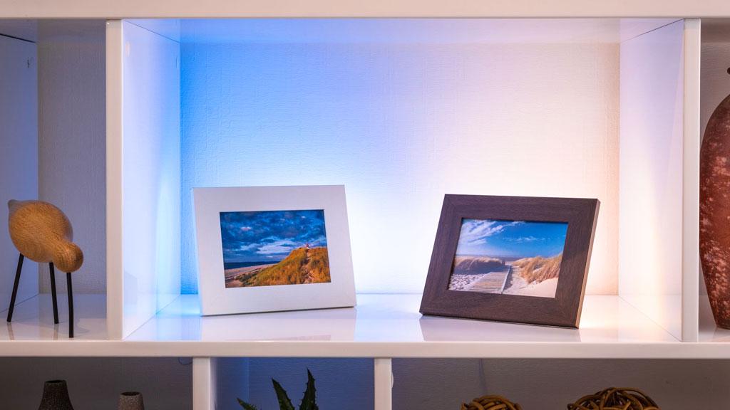 Witte plank met twee fotolijsten in wit en donkerbruin, verlicht met blauw en warm wit licht.