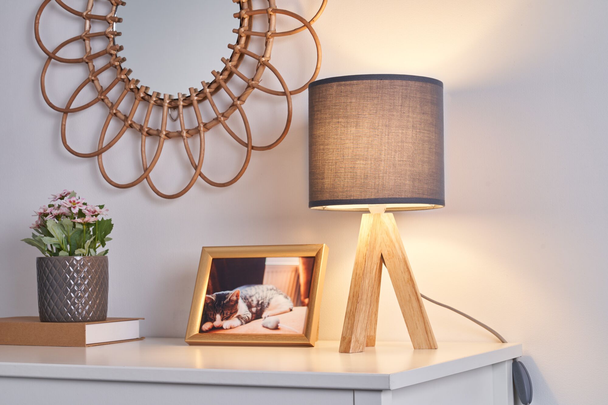 Moderne Tischlampe mit Holzfuß und grauem Stoffschirm auf weißem Sideboard mit Dekoration.