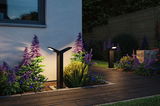 Black metal LED outdoor lights illuminate garden path with purple and blue flowers at dusk