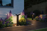 Black metal LED outdoor lights illuminate garden path with purple and blue flowers at dusk