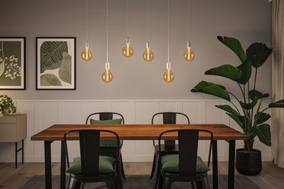 Modern dining area with wooden table, black metal chairs, and warm LED bulb pendant lights.