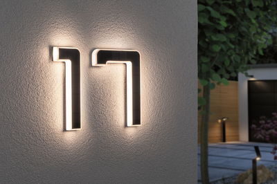 Modern LED house number 17 in black material with warm white light mounted on exterior wall.