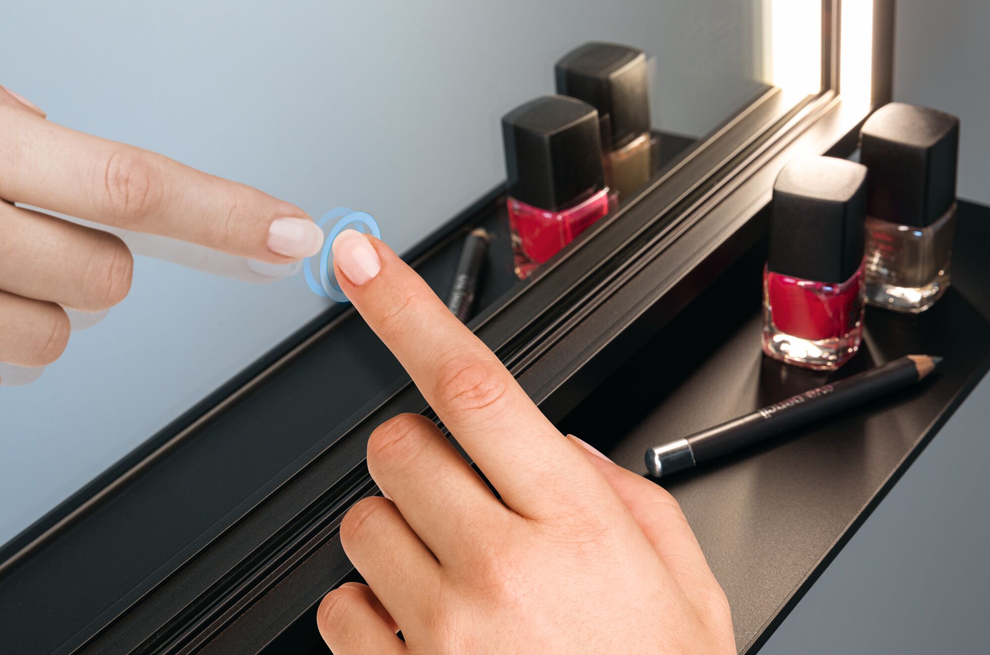 Hand touching black touch switch near nail polish and eyeliner pencil on black shelf with mirror.