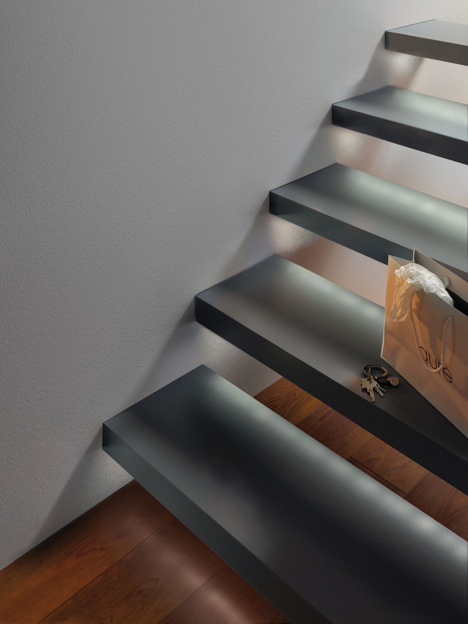 Escalier flottant moderne en métal noir mat avec éclairage mural indirect et sol en bois en dessous.