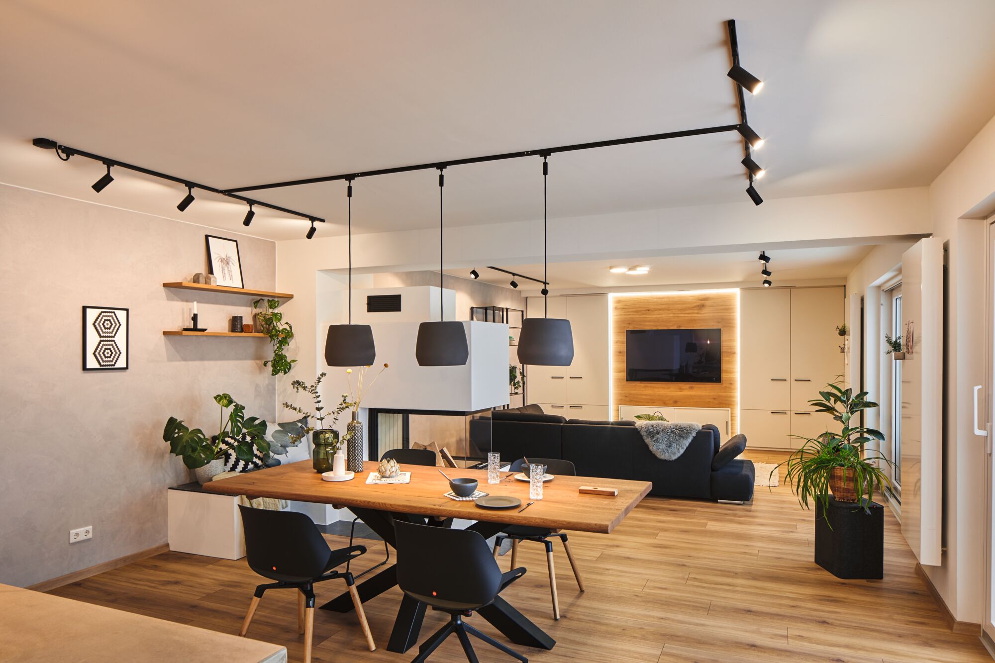 Modernes Wohnzimmer mit Holzfußboden, schwarzem Sofa, Esstisch aus Holz und schwarzen Pendelleuchten