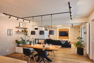 Salon moderne avec sol en bois, canapé noir, table à manger en bois et suspensions noires