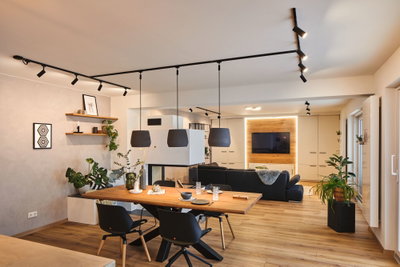 Salon moderne avec sol en bois, canapé noir, table à manger en bois et suspensions noires