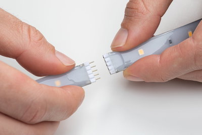 Two hands connecting flexible LED strips with grey silicone coating for modular LED lighting setup