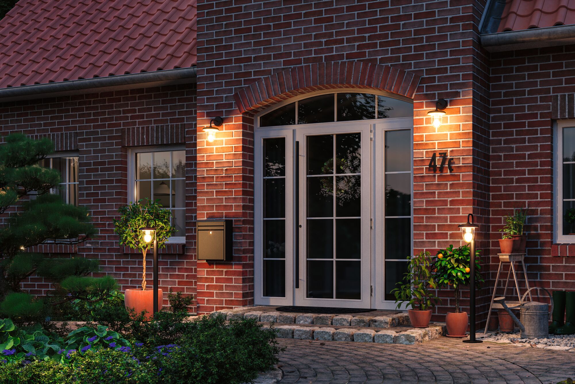 Außenbeleuchtung mit warmweißem Licht an rotem Backsteinhaus mit weißen Türen und Pflanzen im Eingangsbereich