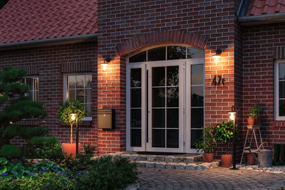 Outdoor lighting with warm white light on red brick house with white doors and plants at entrance