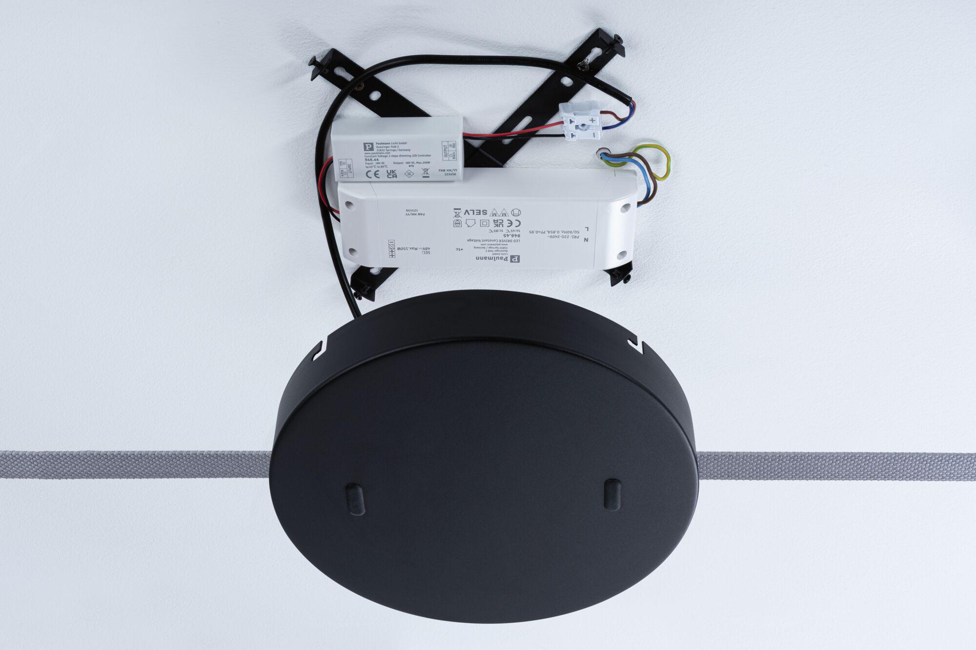 Schwarze LED-Treiberbox aus Kunststoff mit Kabeln und Montageplatte an weißer Wand montiert