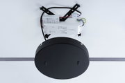 Schwarze LED-Treiberbox aus Kunststoff mit Kabeln und Montageplatte an weißer Wand montiert