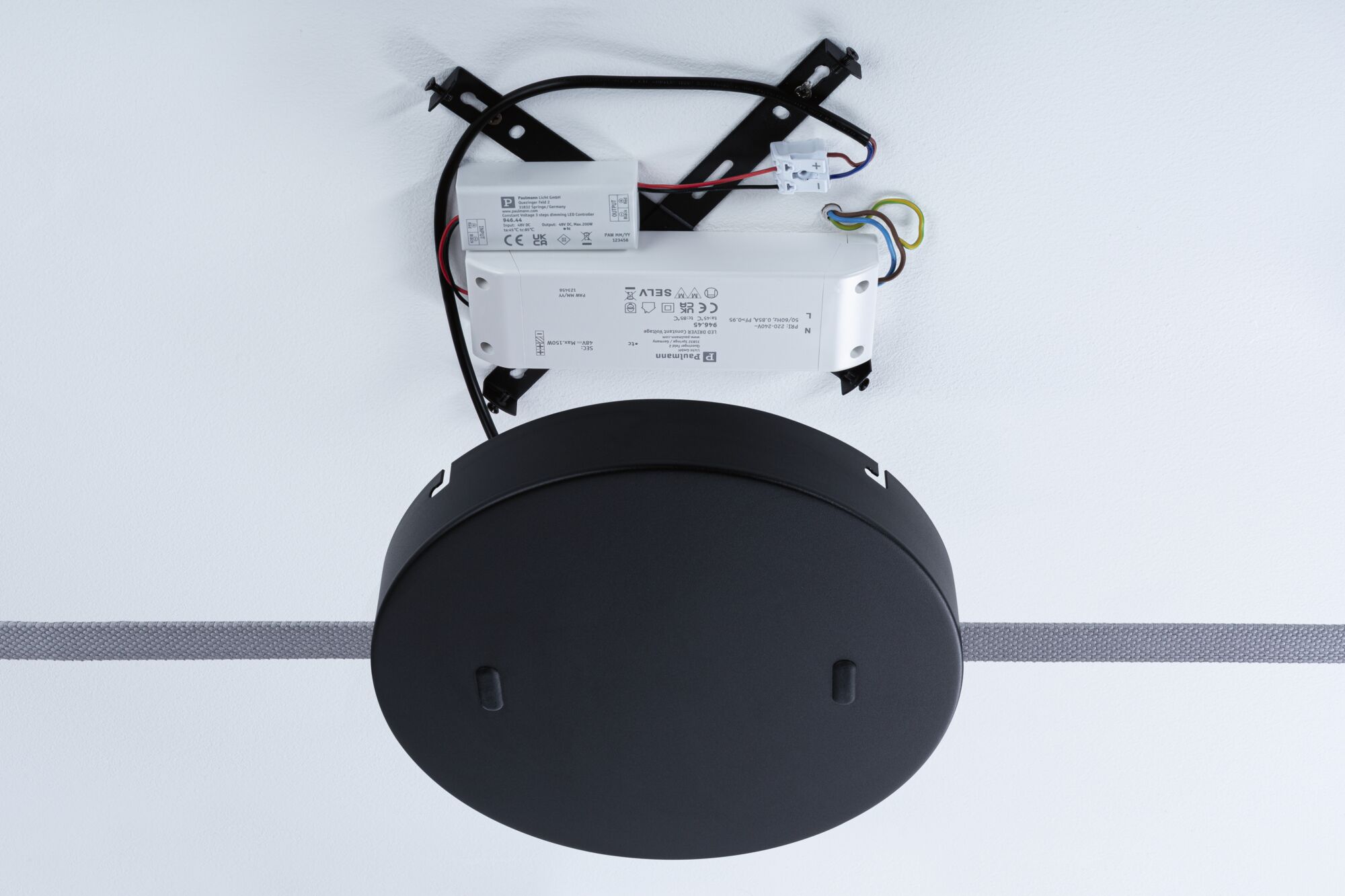 Zwarte kunststof LED-driverbox met kabels en montageplaat bevestigd aan witte muur