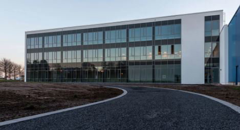 Modern office building with large glass windows and white facade, surrounded by asphalt path.