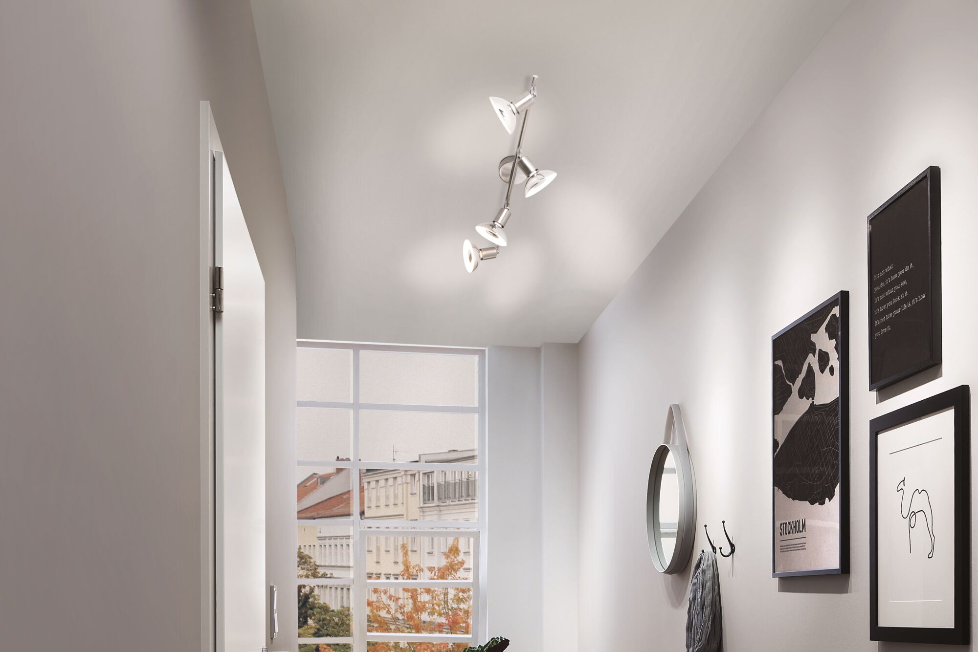 Modern ceiling spotlight in brushed metal with four adjustable lamps in hallway with window view.