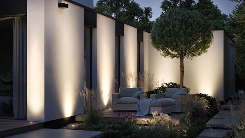 Moderne Außenbeleuchtung an weißer Hauswand mit warmem Licht und gemütlicher Terrasse mit Sitzmöbeln und Pflanzen