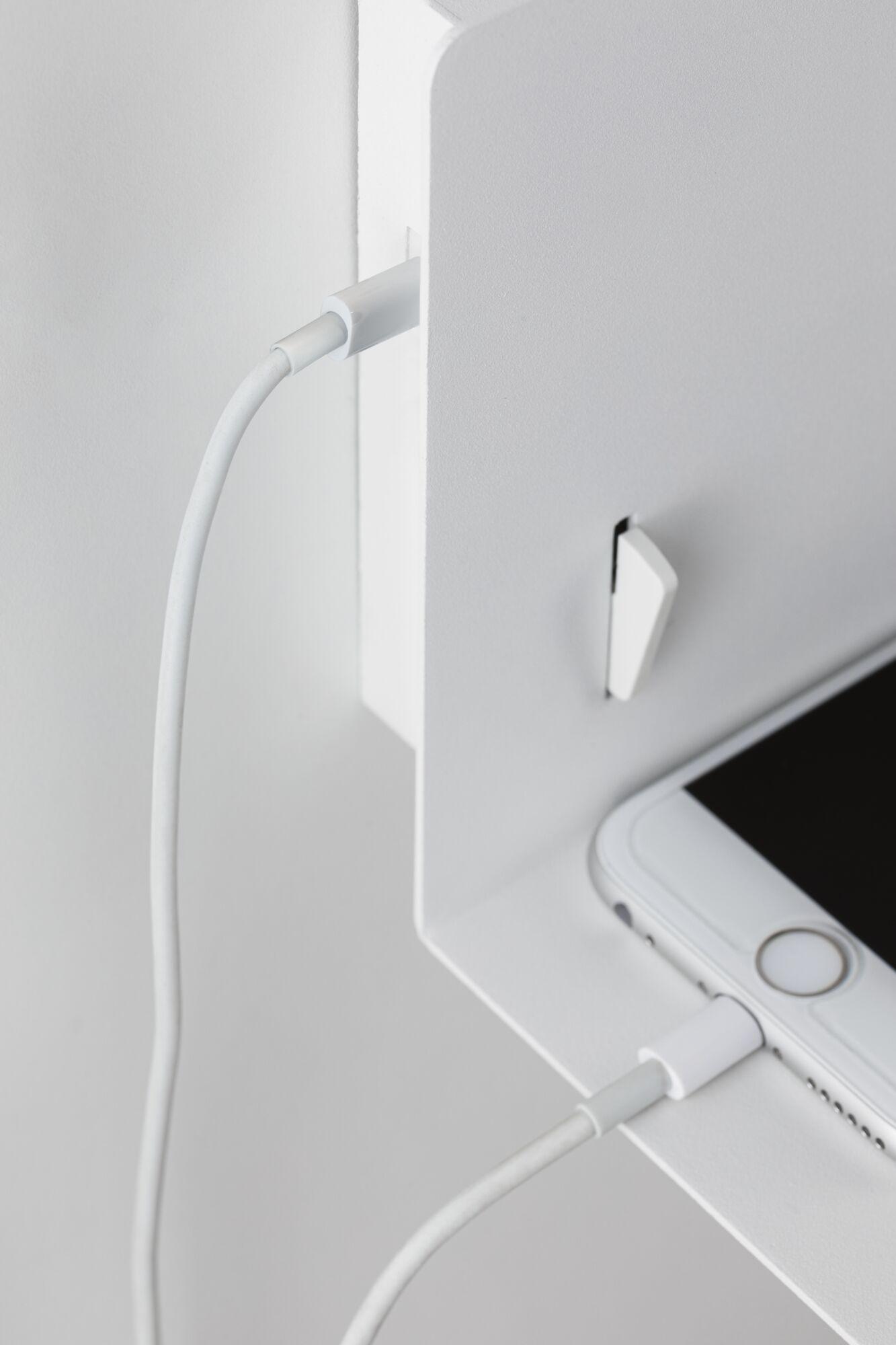 White smartphone charging with cable on white metal shelf, modern minimalist setup