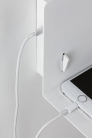 White smartphone charging with cable on white metal shelf, modern minimalist setup