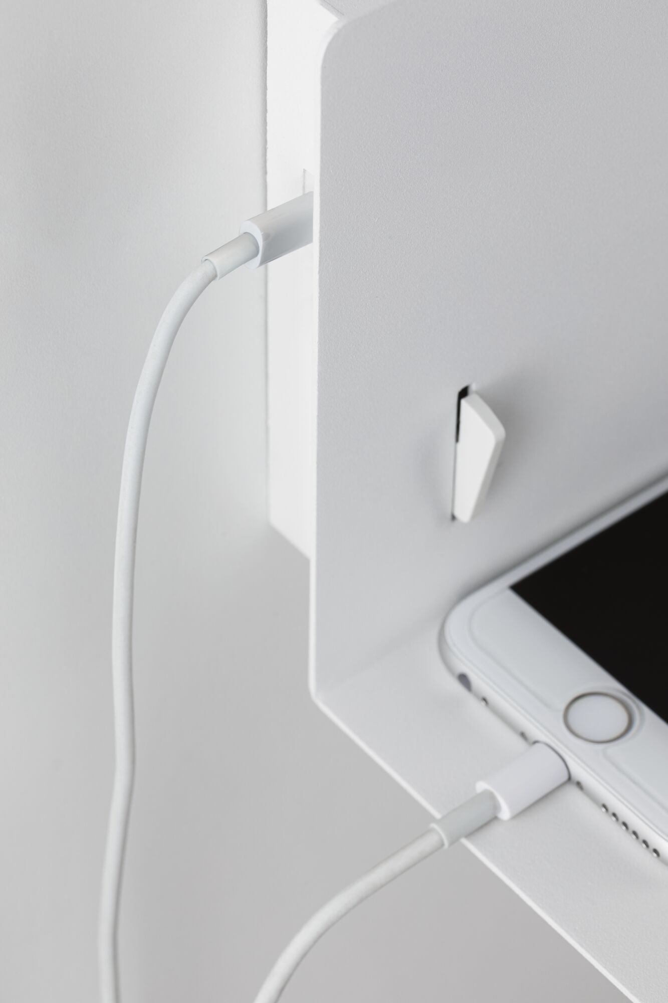 Smartphone blanc en charge avec câble sur étagère métallique blanche, design minimaliste