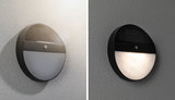 Round black solar wall light with motion sensor, shown mounted on wall day and night