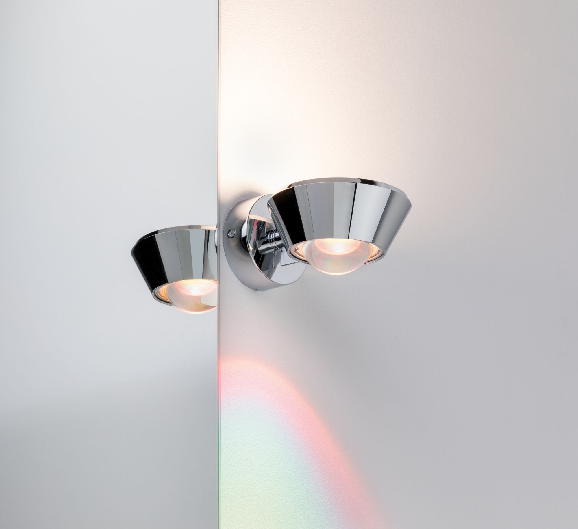 Modern wall spotlight in chrome metal with warm white light and mirror reflection effect.