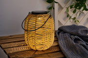 Rattan lantern with black handle and warm light on wooden table next to patterned fabric