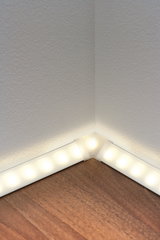LED-Bodenleistenbeleuchtung mit warmweißem Licht an weißer Wand und Holzboden für indirekte Raumbeleuchtung