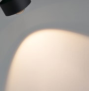 Schwarze LED-Wandleuchte aus Metall mit warmweißem Lichtschein an grauer Wand