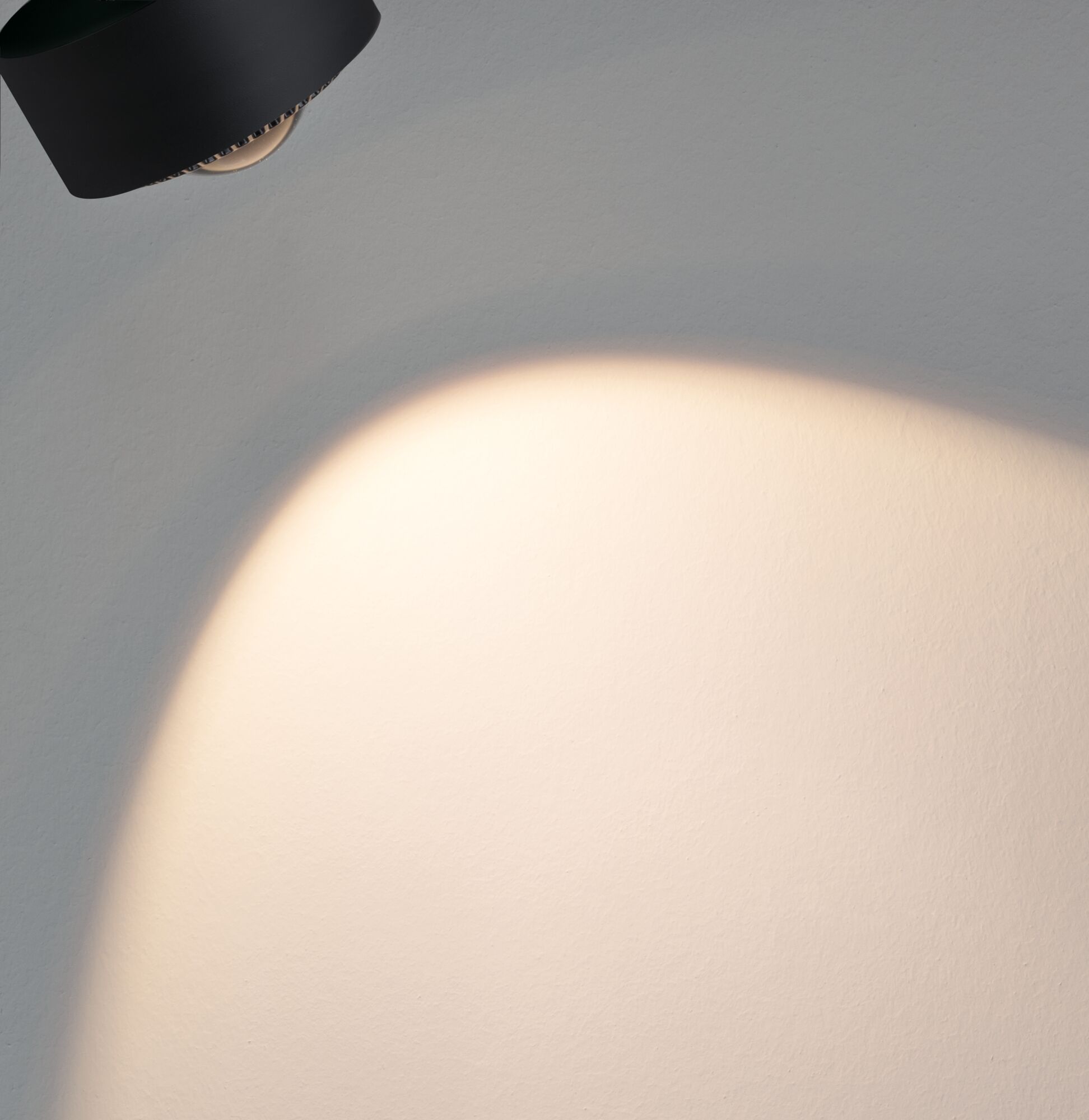 Schwarze LED-Wandleuchte aus Metall mit warmweißem Lichtschein an grauer Wand