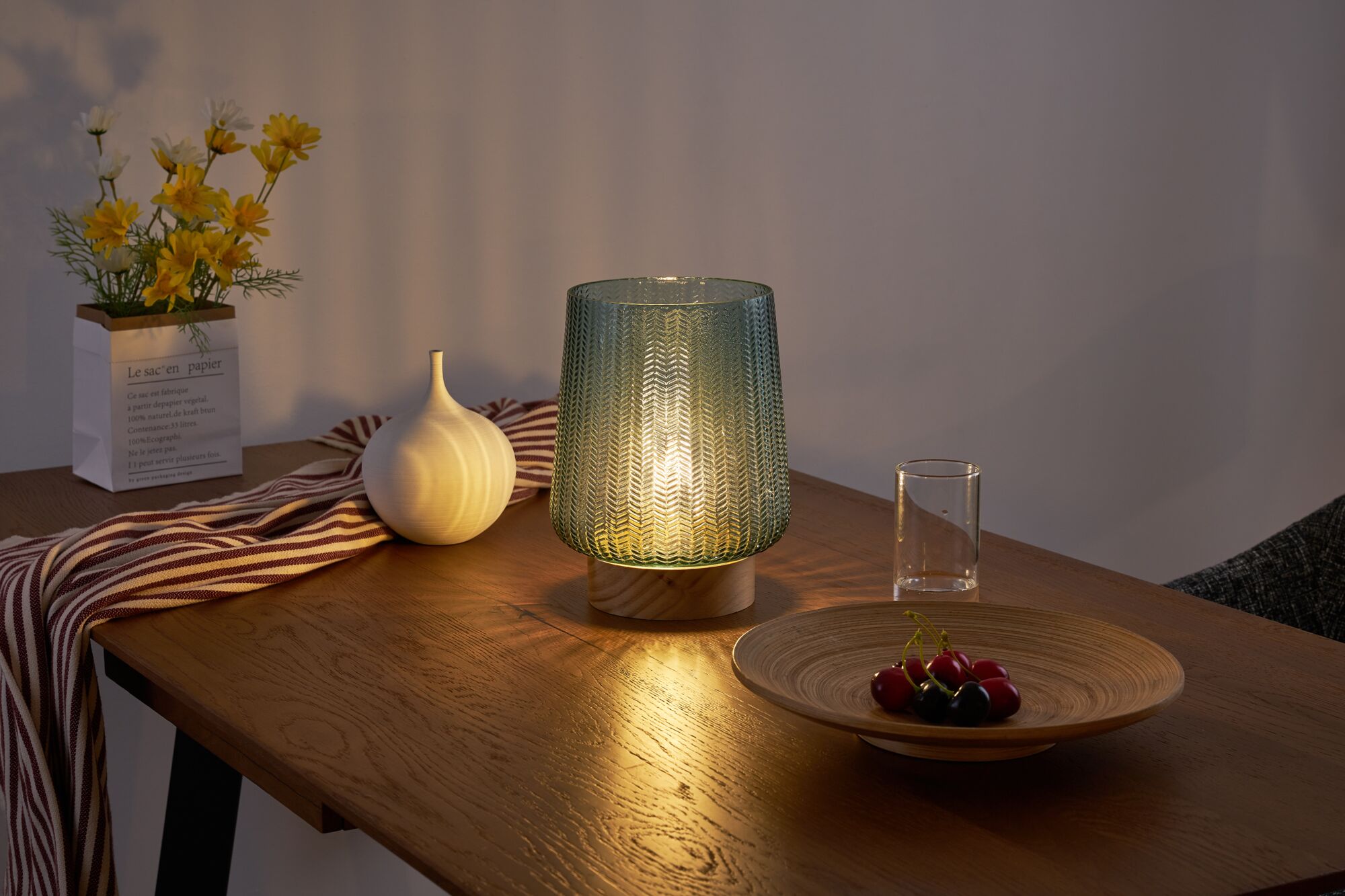 Grüne Glas-Tischleuchte mit Holzfuß auf Holztisch mit Dekoration und warmem Licht.