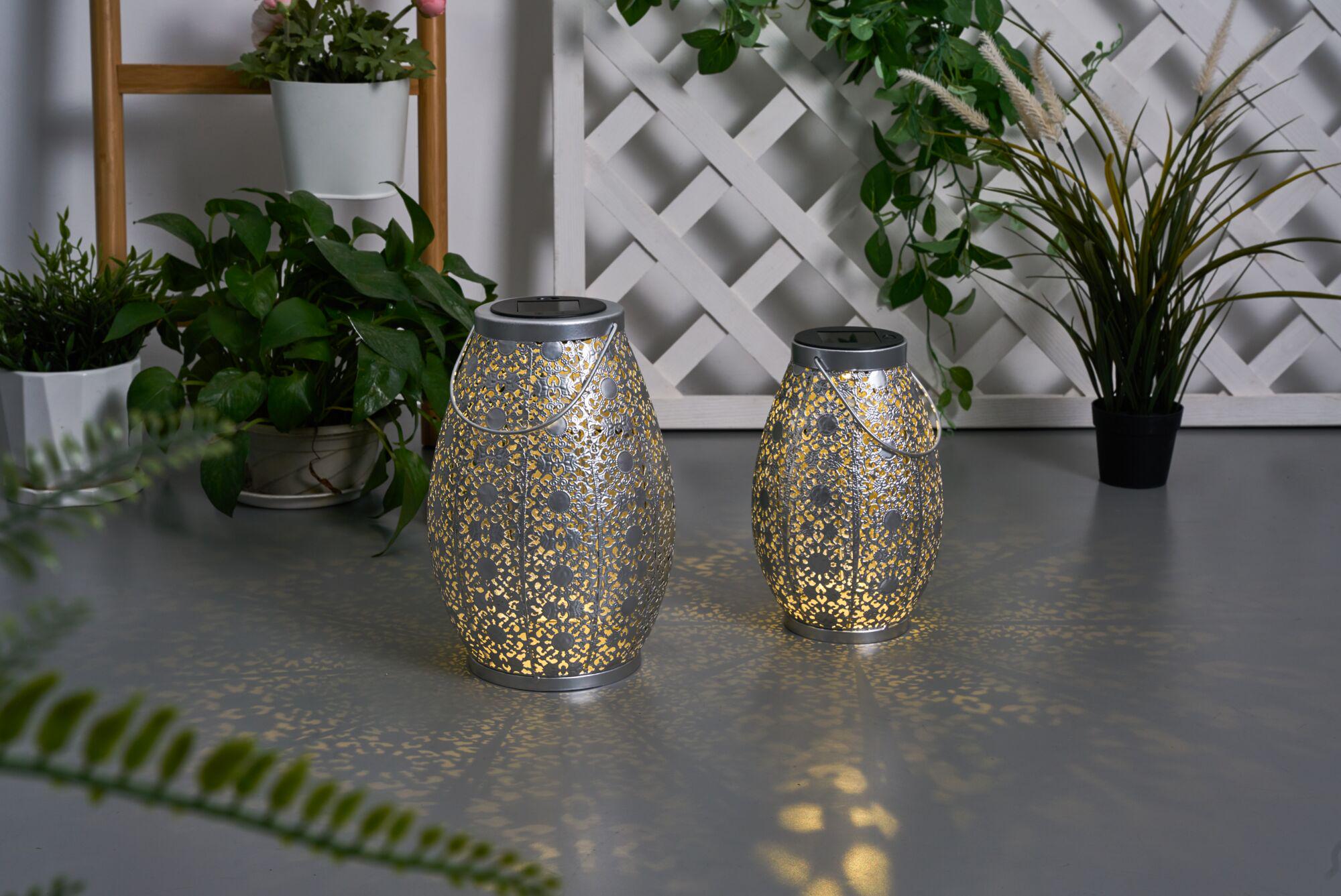 Two silver metal lanterns with intricate pattern and warm light, decorative indoor lighting.
