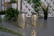 Two silver metal lanterns with intricate pattern and warm light, decorative indoor lighting.